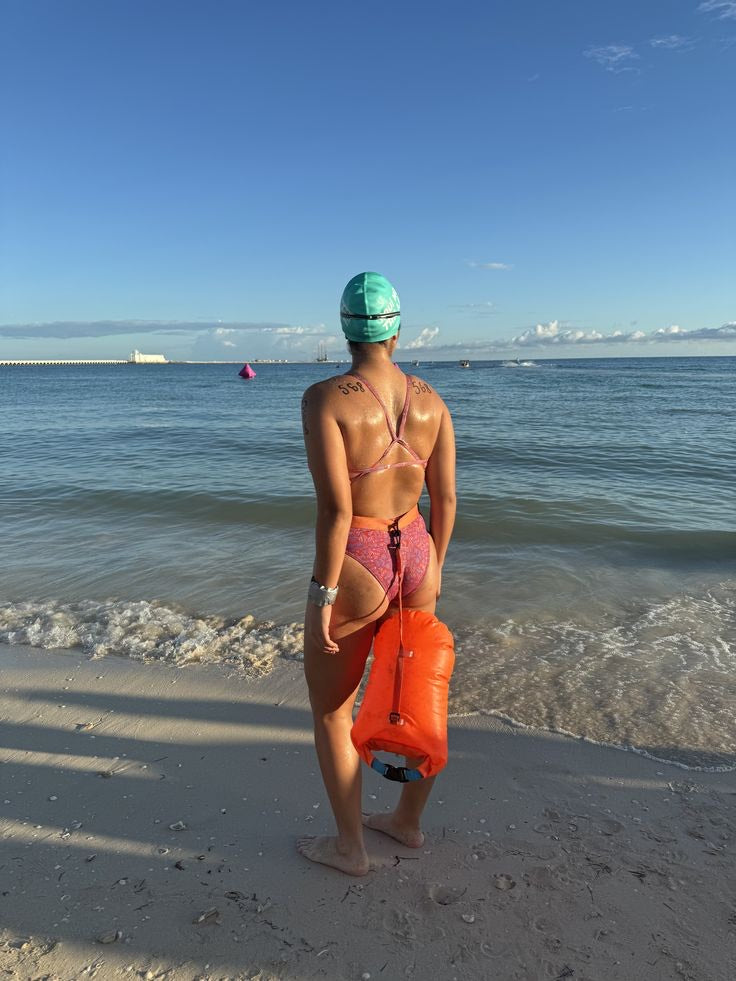 Swimmer at the shoreline holding an orange dry-bag buoy