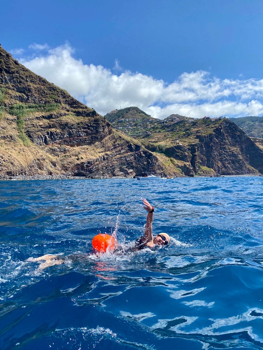 Swimmer with orange tow float beneath sea cliffs
