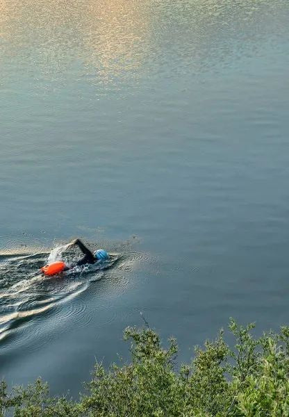 Lone swimmer with orange float on a calm lake